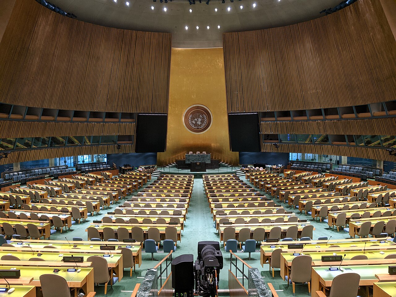 The UN General Assembly Hall seen from the back, with rows of empty delegate desks.
