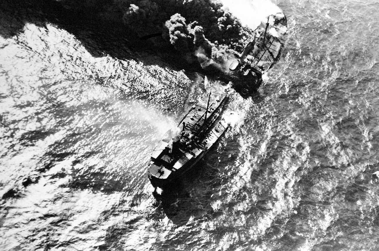 An oil tanker burns at sea after being struck, showing the scale of the vessel and extent of fire.
